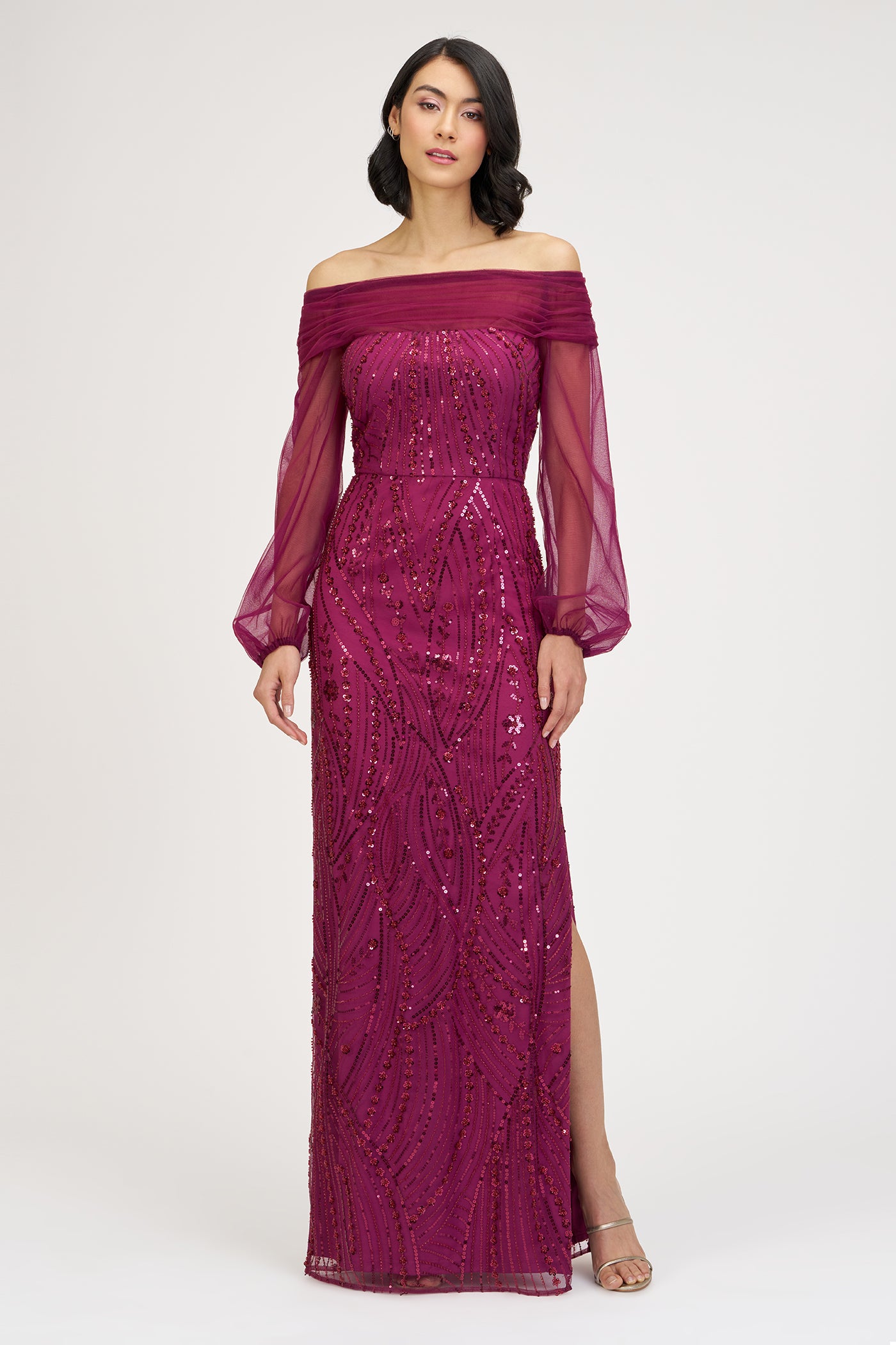 Woman wearing a burgundy off-shoulder gown with intricate detailing on a white background