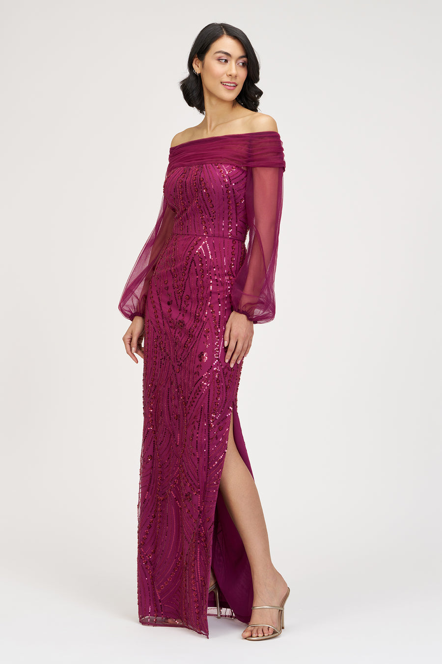 Woman wearing a magenta off-shoulder dress with sheer sleeves on a white background