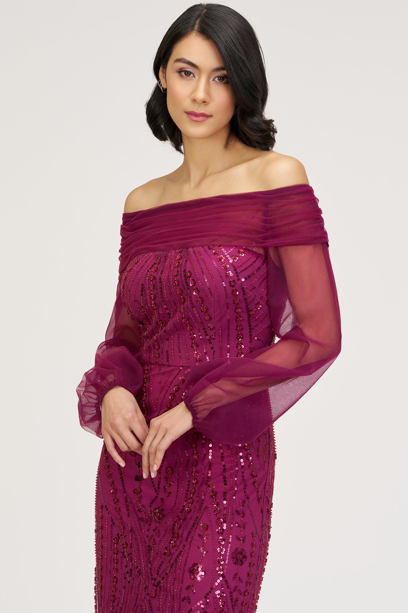 Woman wearing a magenta off-shoulder dress with sequin detailing on a light gray background