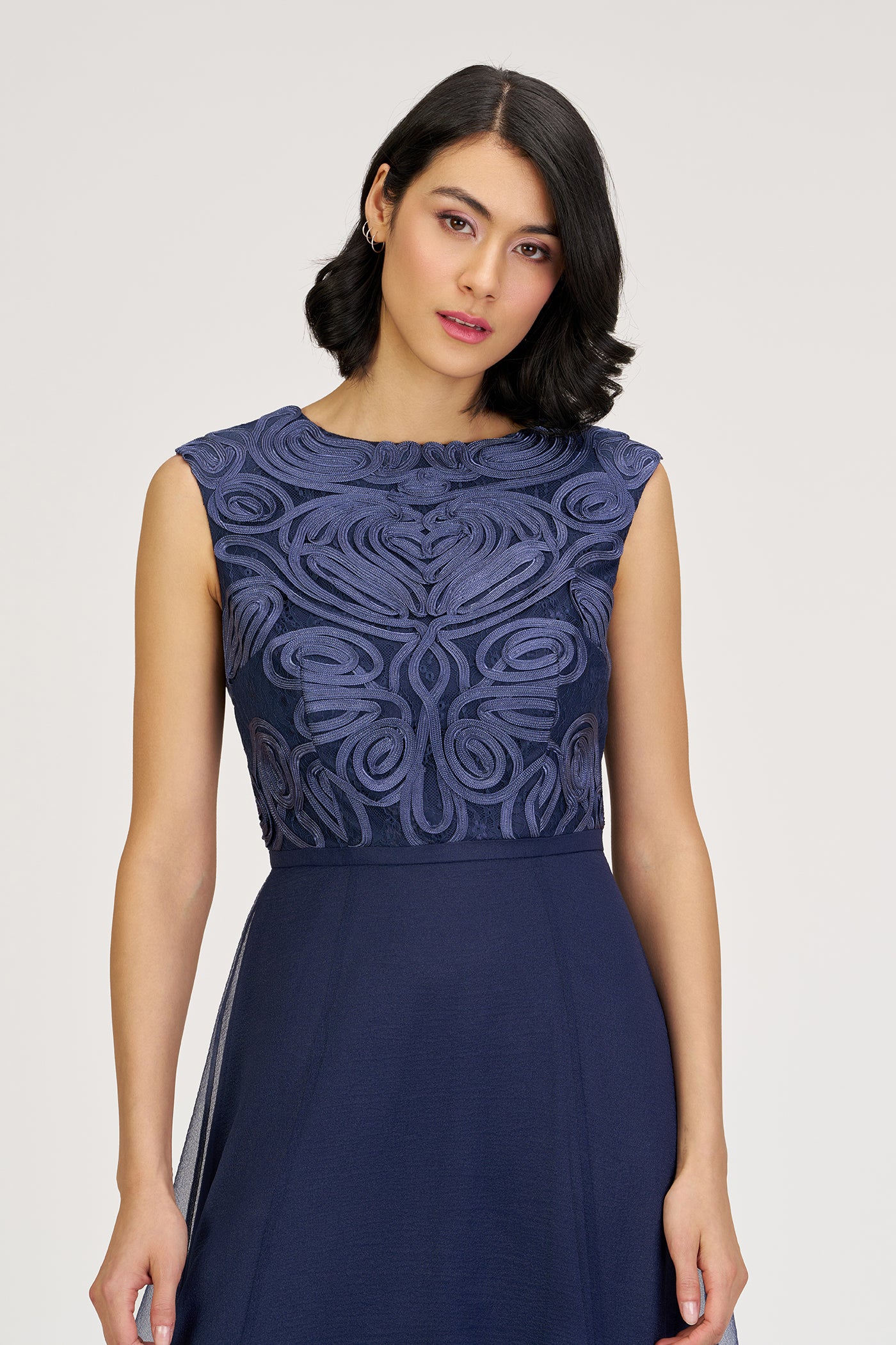 Woman wearing a navy blue dress with intricate lace detailing on a white background