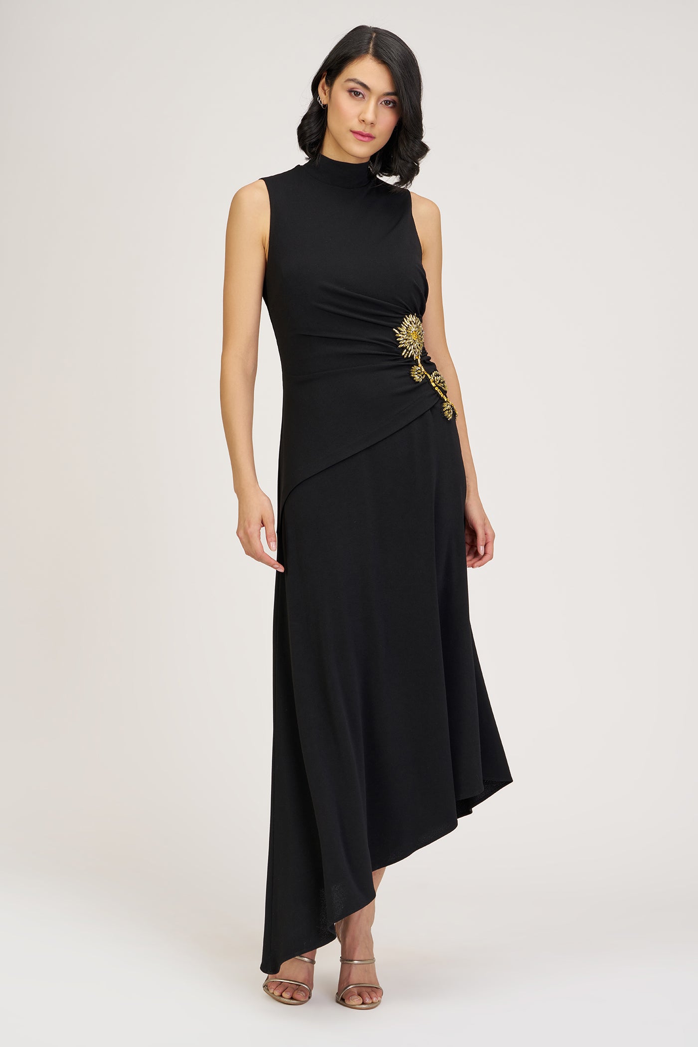 Woman wearing a black sleeveless dress with a gold embellishment on a white background