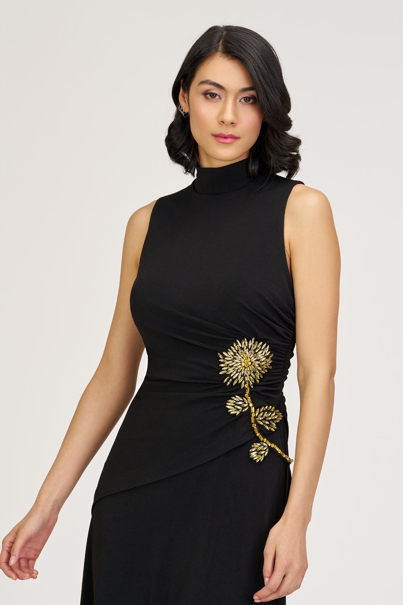 Woman wearing a black dress with gold floral embroidery on a white background