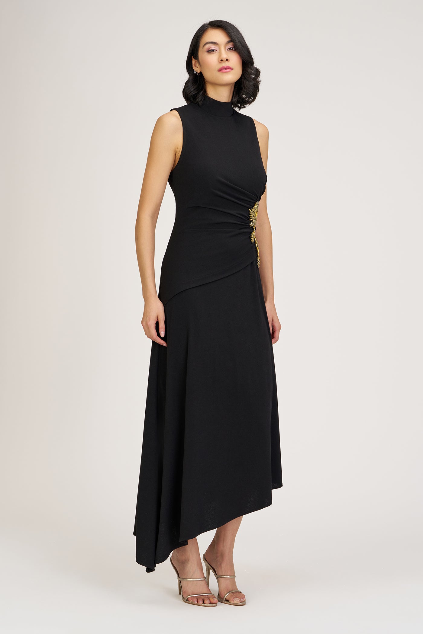 Woman wearing a black sleeveless dress with a high neckline and draped design on a white background