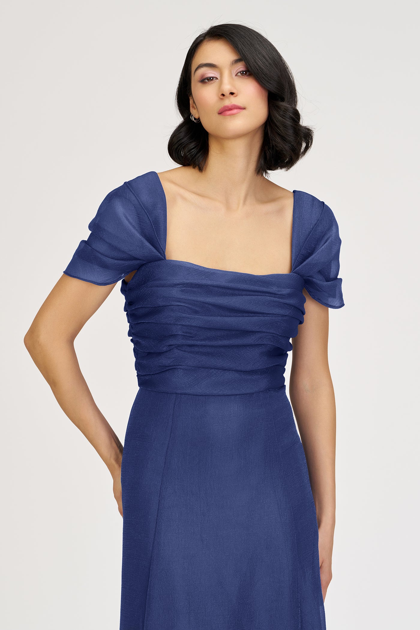 Woman wearing a blue dress with ruched bodice on a white background