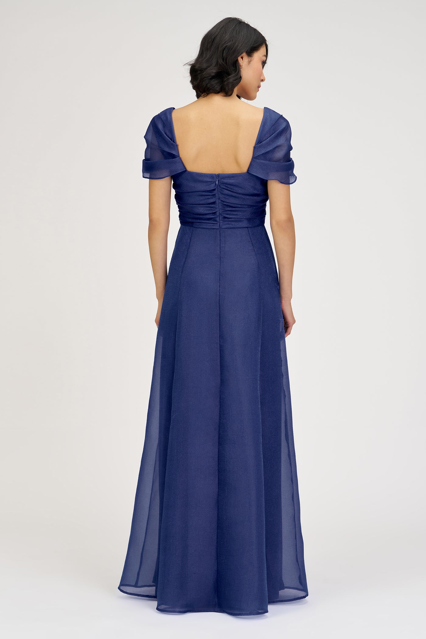 Woman wearing a long blue dress with open back on a white background