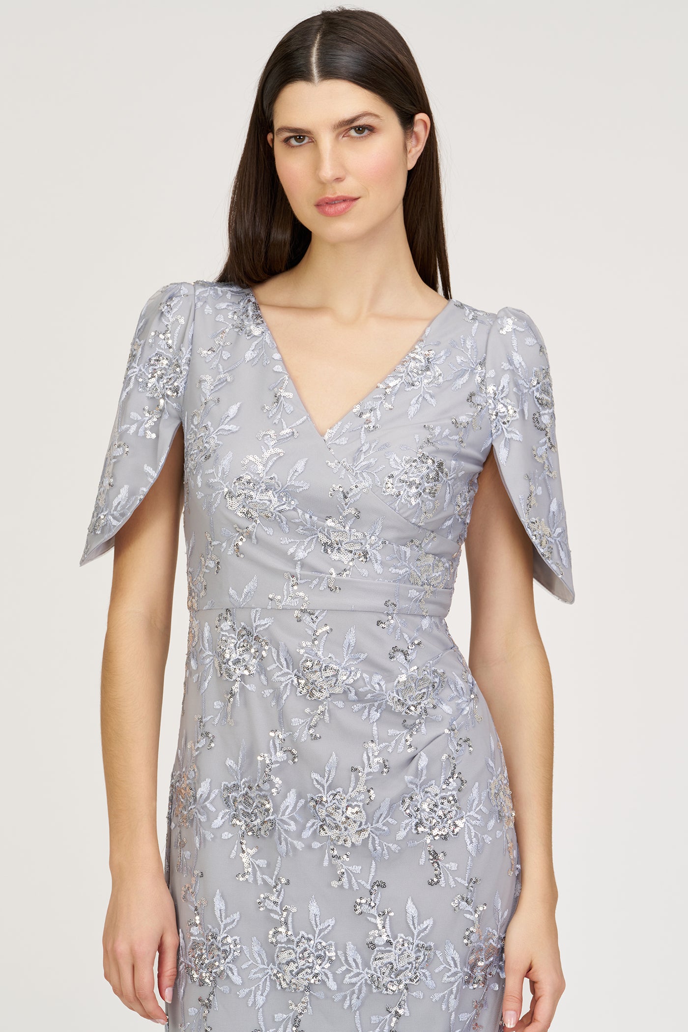 Woman wearing a silver evening gown with floral embroidery on a white background